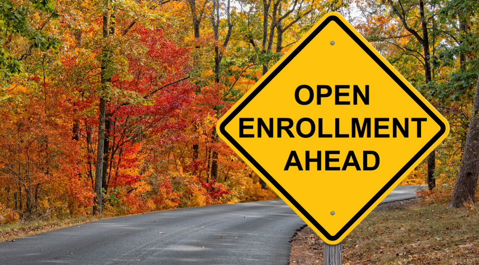 an image of a road sign that says "open enrollment ahead." The sign is just before a curve in the road. There is beautiful fall foliage all around.